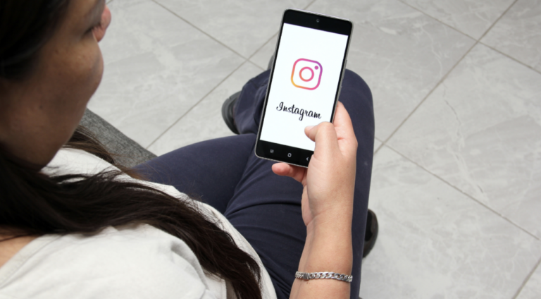 A woman sitting down and looking at an open Instagram app on her smartphone screen, perfectly illustrating a patient discovering social media wellness trends.
